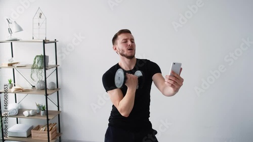 Vain sport. Posing man. Fitness blogging. home training. Funny selfish athletic guy making selfie with dumbbells in hand on mobile phone playing fancy in light room interior. photo