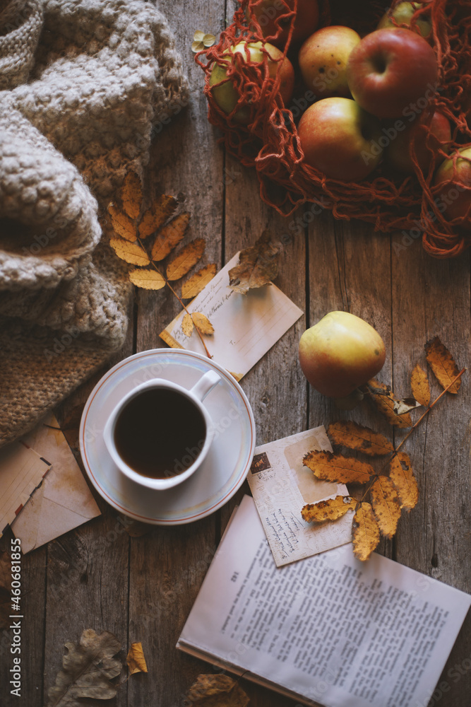 A cup of coffee on a wooden background, apples in a bag are on the table.