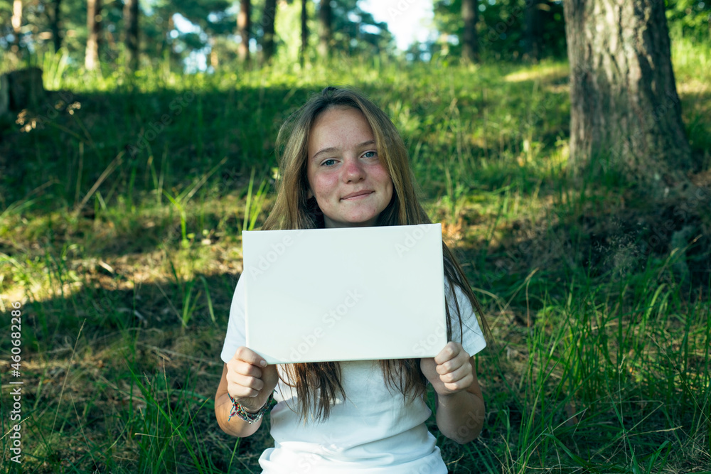 Teen girl holding clean white sheet paper (for your message), in the park. Teen girl holding clean white sheet paper (for your message), in the park.