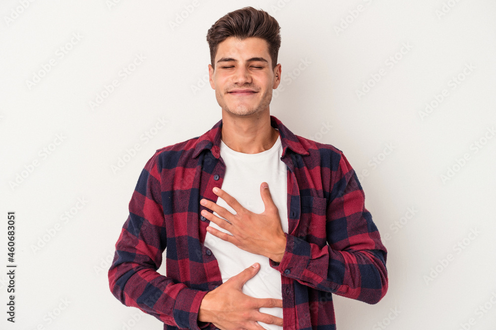 Young caucasian man isolated on white background laughs happily and has fun keeping hands on stomach. Young caucasian man isolated on white background laughs happily and has fun keeping hands on stomach.