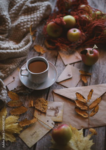 A cup of coffee stands on a wooden background  apples and autumn leaves are on the table.