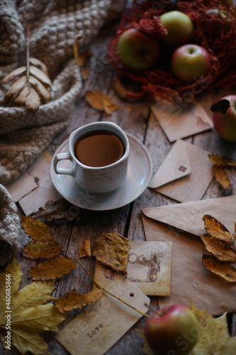 A cup of coffee stands on a wooden background, apples and autumn leaves are on the table.
