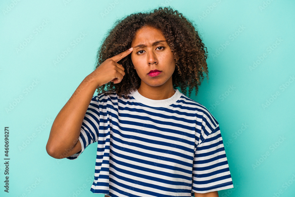 Young african american woman with curly hair isolated on blue background pointing temple with finger, thinking, focused on a task. Young african american woman with curly hair isolated on blue background pointing temple with finger, thinking, focused on a task.