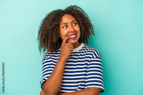 Young african american woman with curly hair isolated on blue background relaxed thinking about something looking at a copy space. © Asier