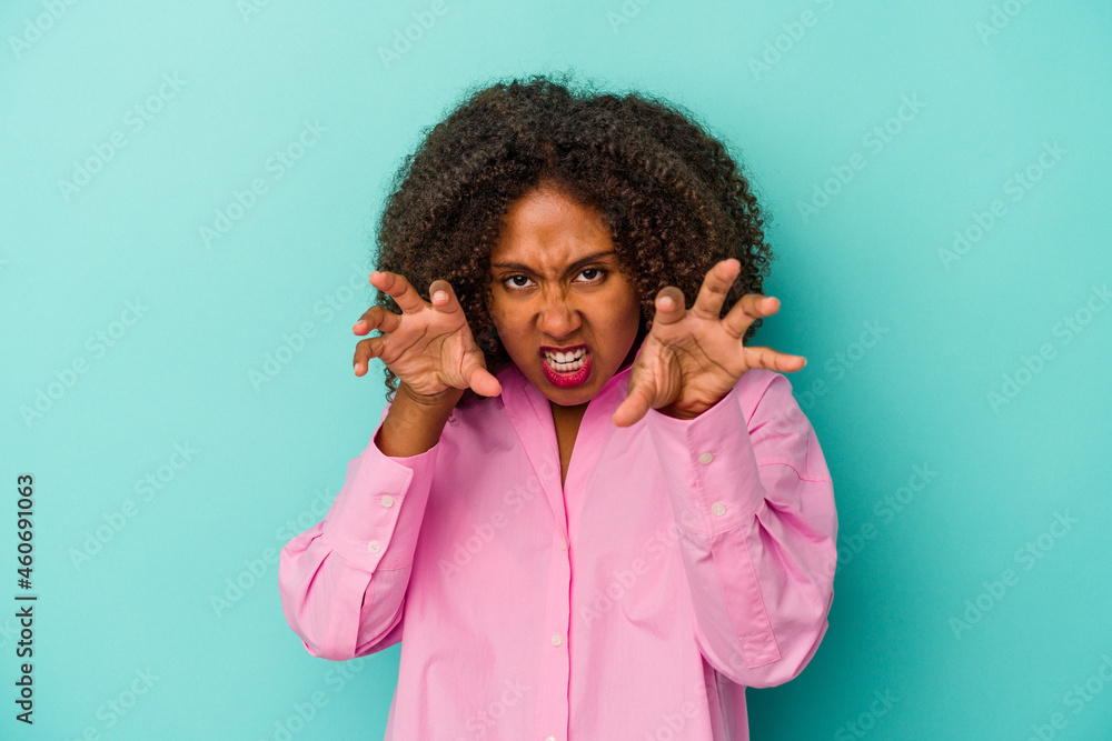 Young african american woman with curly hair isolated on blue background upset screaming with tense hands. Young african american woman with curly hair isolated on blue background upset screaming with tense hands.