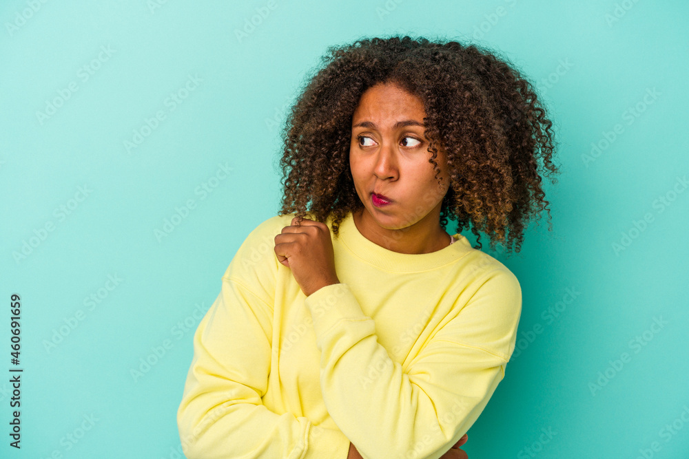 Young african american woman with curly hair isolated on blue background confused, feels doubtful and unsure.