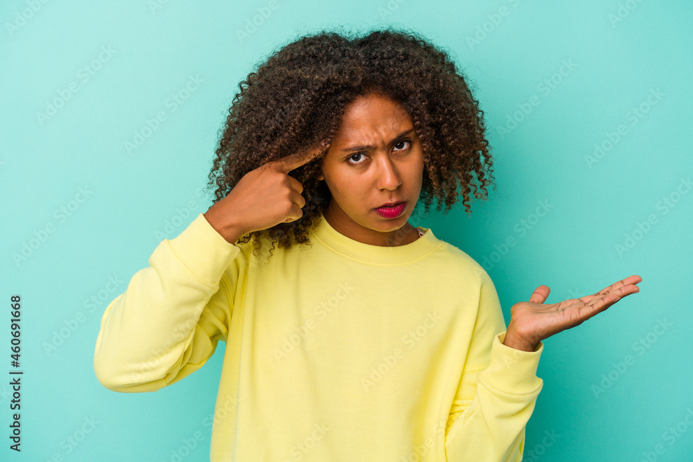 Young african american woman with curly hair isolated on blue background showing a disappointment gesture with forefinger. Young african american woman with curly hair isolated on blue background showing a disappointment gesture with forefinger.