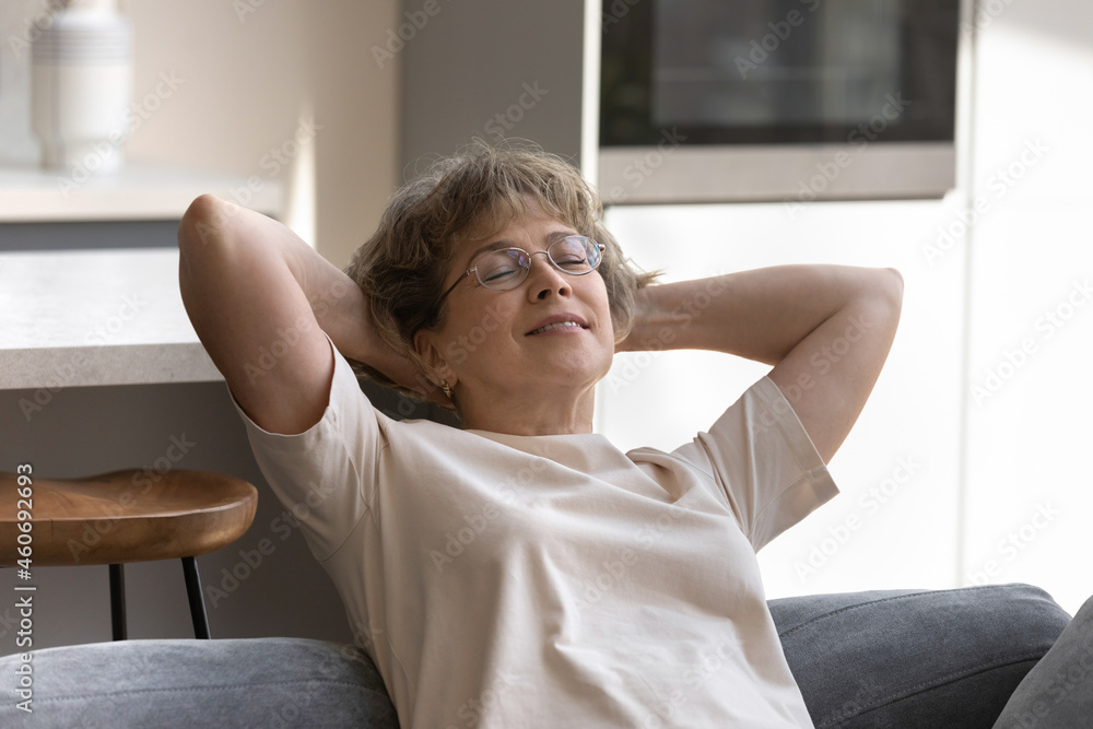 Happy relaxed middle aged senior retired woman in eyeglasses sleeping meditating on cozy sofa with folded hands behind head, enjoying peaceful leisure weekend time alone at home, recreation concept. Happy relaxed middle aged senior retired woman in eyeglasses sleeping meditating on cozy sofa with folded hands behind head, enjoying peaceful leisure weekend time alone at home, recreation concept.