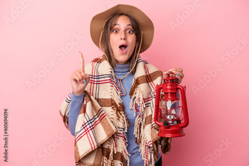 Young caucasian woman holding vintage lantern isolated on pink background having an idea, inspiration concept.