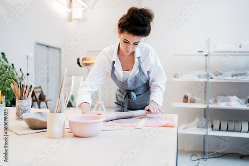 A professional craftsman makes dishes from ceramics. A uniformed employee in a decorative products studio. A ceramist makes a plate out of porcelain. A woman in an apron works in a pottery workshop. photo