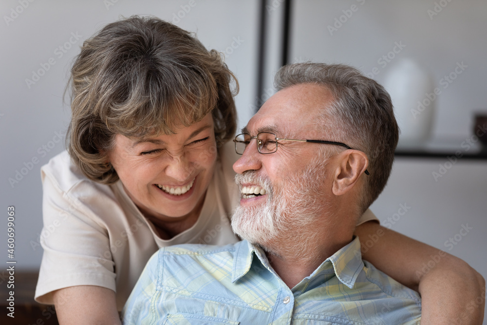 Head shot caring happy older woman cuddling joyful mature husband, laughing together at funny joke, enjoying pleasant conversation during carefree leisure weekend time at home, relations concept. - obrazy, fototapety, plakaty 