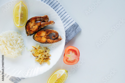 Wallpaper Mural Fried fish with onions, rice and lemon lies on a plate, on a waffle towel and cutlery on a white background. Torontodigital.ca