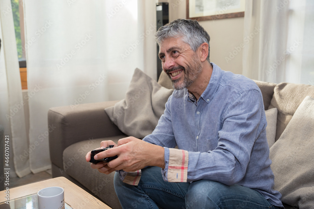 Un homme d'âge mur de 50 ans tient une manette de jeux vidéo dans ses mains et s'amuse en jouant à la console, il a le sourire