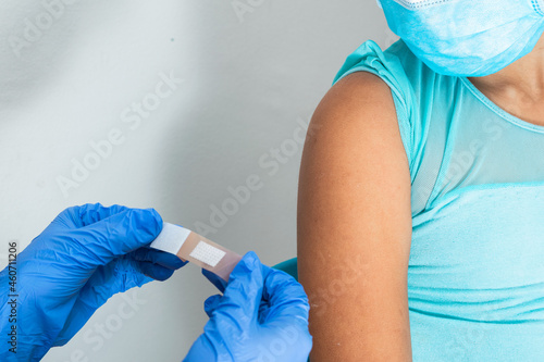 Doctor in blue rubber protective gloves putting an adhesive bandage on a girl's arm after hurting her skin or injecting vaccine. First aid. Medical, pharmaceutical and sanitary concept.