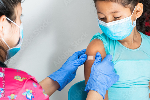 Doctor in blue rubber protective gloves putting an adhesive bandage on a girl's arm after hurting her skin or injecting vaccine. First aid. Medical, pharmaceutical and sanitary concept. Close-up.