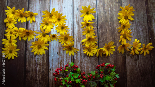 Autumn concept, word "autumn" laid out with yellow flowers on wooden background decorated with berries