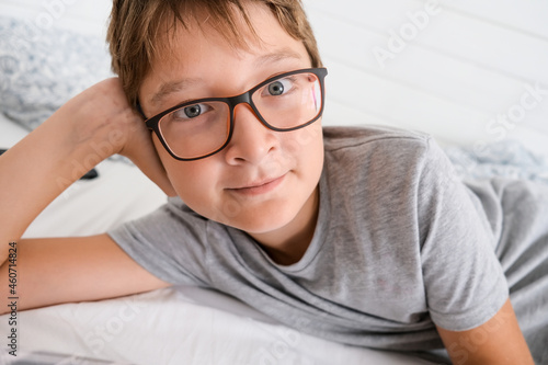 A lazy cheerful happy boy wearing glasses lying in bed and resting, because he is not in school during lockdown or quarantine