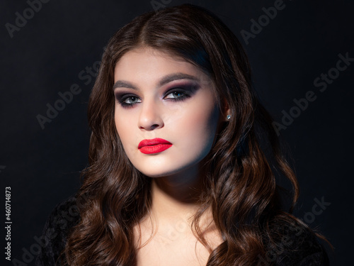 Gorgeous young brunette in a chic evening look. Scarlet lips and eye shadow, wave hair styling. luxury close-up portrait