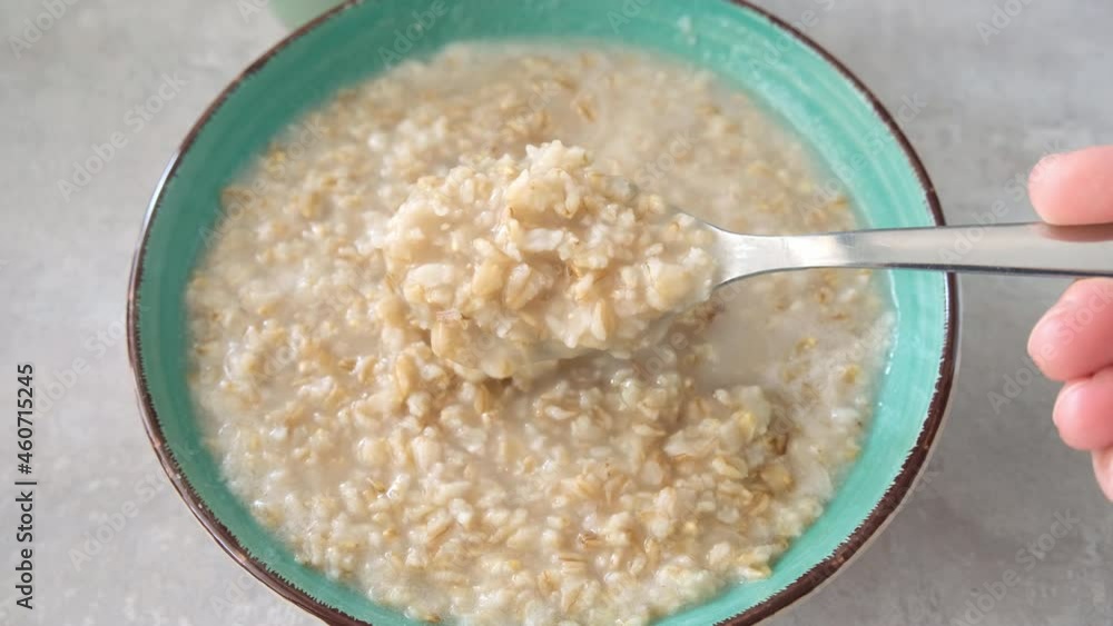 A hand stiring cooked oats porridge with a spoon in a green bowl, healthy breakfast and dieting product close up, tasty vegan food A hand stiring cooked oats porridge with a spoon in a green bowl, healthy breakfast and dieting product close up, tasty vegan food