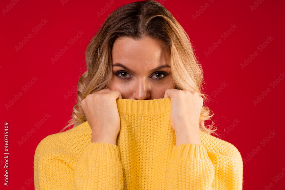 young sweet and smiling blonde woman in a yellow knitted sweater on a red background, wrapped in a collar young sweet and smiling blonde woman in a yellow knitted sweater on a red background, wrapped in a collar