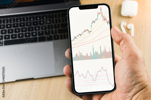 Financial stock market graph on the smartphone screen on wooden background with a computer beside it. Stock Exchange. photo