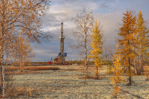 Northern taiga in autumn. Golden yellow palette. Landscape at the oil and gas field. A drilling rig stands between the trees as the central element of the composition