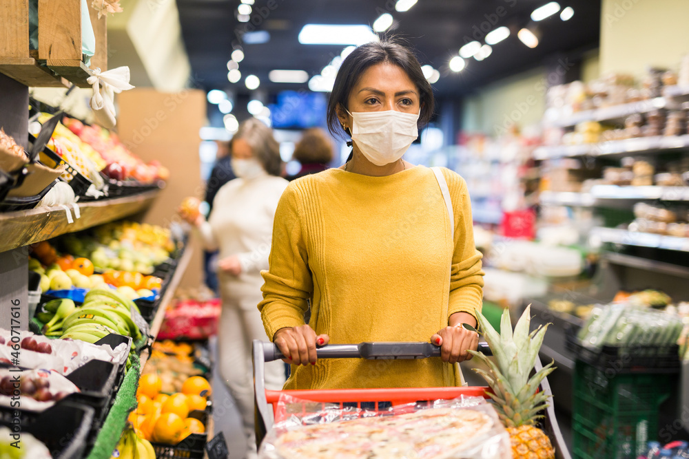 Casual woman in protective mask doing shopping in grocery department of supermarket