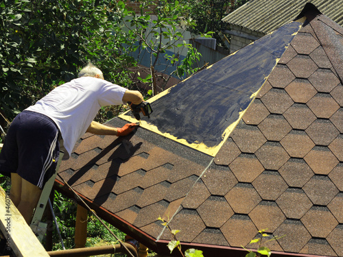 the roofer works with a screwdriver on the roof of the gazebo photo