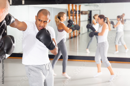 Sports determined Hispanic man mastering self defense techniques, practicing punches at boxing gym