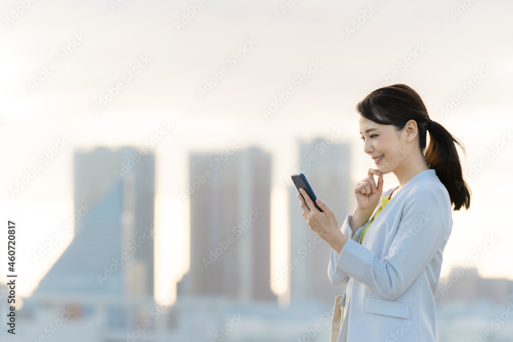 都市を背景にスマホを見る女性