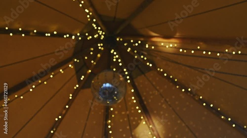 Party tent interior with disco ball hanging and reflecting light surrounded by LED fairy lights. 50 fps slow orbit and rack focus. photo