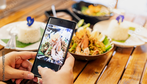 Female hand uses the Mobile Phone take photo with the Thai food for recommending and share to social media.