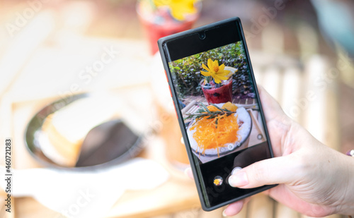 Female hand uses the Mobile Phone take photo with the Thai dessert to recommend and share to social media.
