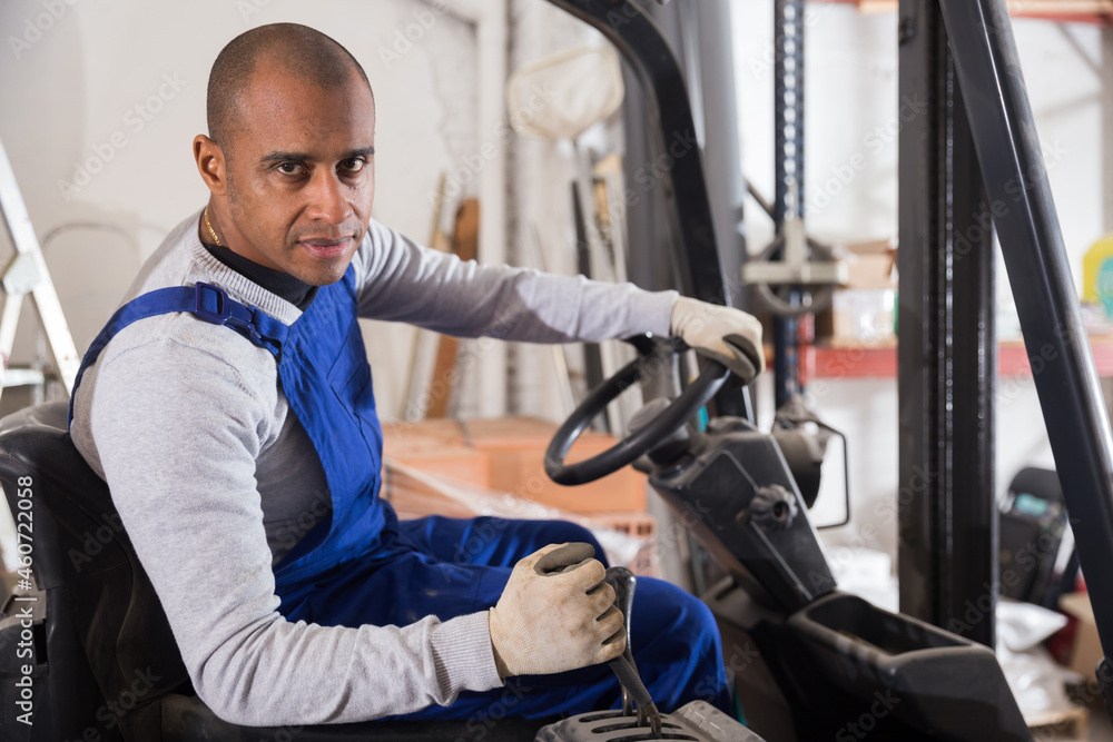 Portrait of confident hispanic worker driving forklift in building materials store