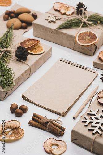 Gift boxes wrapped reusable craft paper, decorated dried fruits, pine cones, fir branches and blank spiral notebook. Zero wast Christmas composition. Trendy branding mock up. New year gifts mockup.