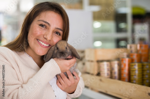 Portrait of smiling young adult woman choosing new pet in store, holding cute rabbit © JackF