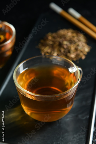 Glass cup of tasty hojicha green tea on black background