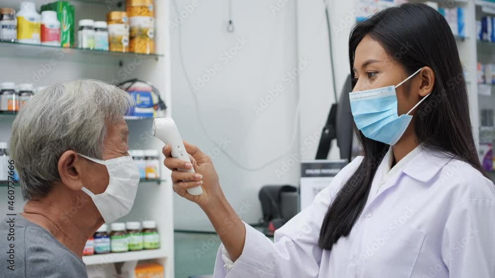 Doctor woman taking a temperature to forehead of elderly woman with a digital thermometer in pharmacy store at hospital. Pharmacist checking temperature with digital detection technology. Doctor woman taking a temperature to forehead of elderly woman with a digital thermometer in pharmacy store at hospital. Pharmacist checking temperature with digital detection technology.