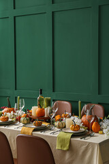 Autumn table setting with fresh pumpkins and flowers near green wall