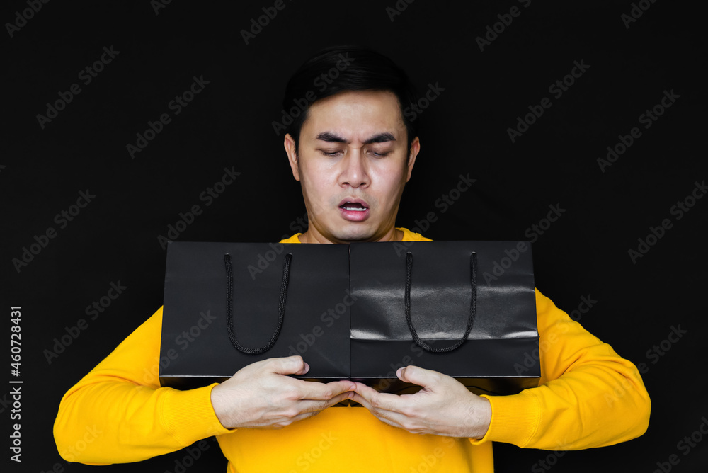 Asian male acting amaze and holding shopping bags on dark background for Black Friday concept. Asian male acting amaze and holding shopping bags on dark background for Black Friday concept.