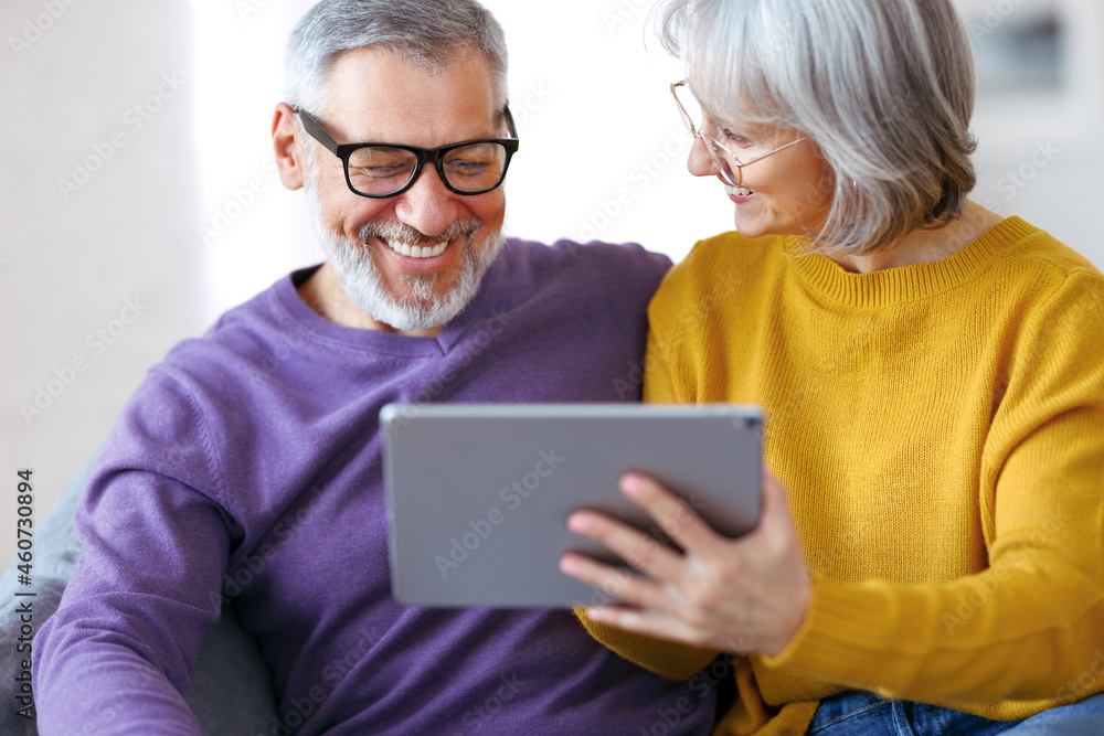 Beautiful mature family couple looking at tablet with smile on face while spending time together Beautiful mature family couple looking at tablet with smile on face while spending time together