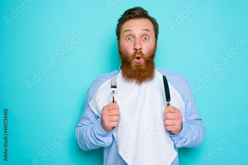 Shocked man with tattoos is ready to eat something with cutlery in hand photo