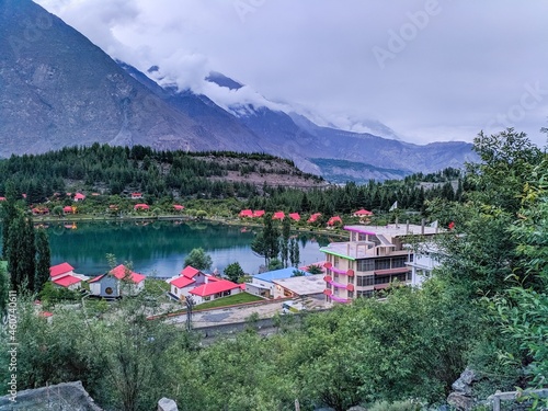 Stunning view of Kalam Valley (Swat, kpk) Pakistan showing restaurants with red roofs surrounding a scenic lake reflecting pines with pine trees and clouds hovering over high mountains in background photo