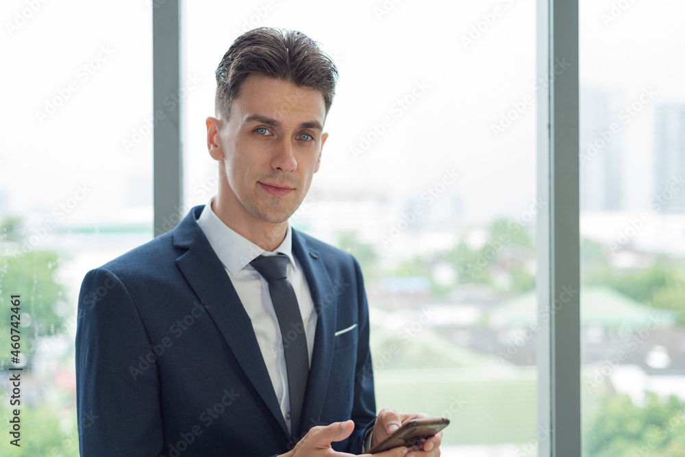 Portrait of adult smart business man in suit outfit standing and using smartphone in modern workplace Portrait of adult smart business man in suit outfit standing and using smartphone in modern workplace