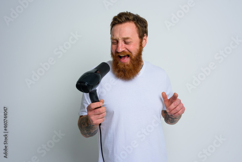 Happy man with beard use hair dryer as microphone and dances