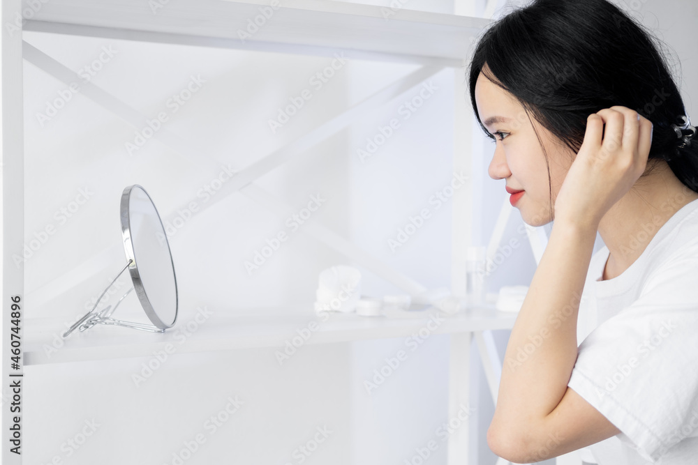 Morning beauty care. Asian woman. Skin treatment. Advertising background. Pretty smiling lady looking round mirror in light room interior copy space. Morning beauty care. Asian woman. Skin treatment. Advertising background. Pretty smiling lady looking round mirror in light room interior copy space.