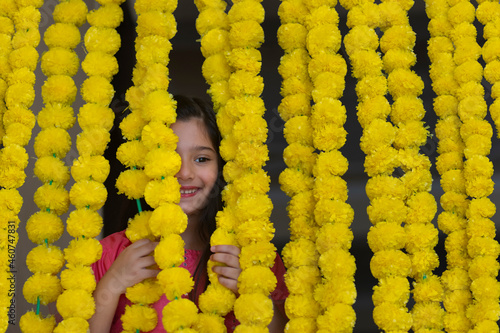 A little girl dressed in traditional wear standing behind festive flower garlands decoration. photo