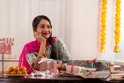 A woman gazing sideways while sitting amidst presents,sweets,Diwali light and festive garland decoration. photo