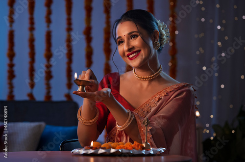 A beautiful woman holding a diya and smiling amidst diwali decoration, lights and a pooja thali. photo