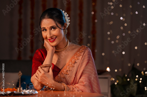 A beautiful woman sitting with hands on chin and smiling amidst diwali decoration, lights and a pooja thali. photo